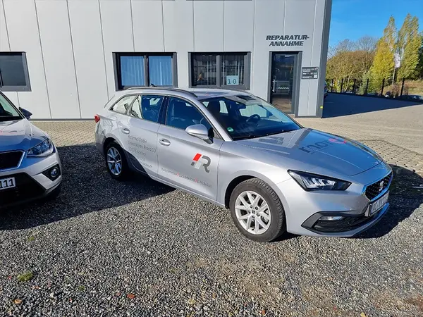 Silberner Kombi mit Firmenlogo steht vor moderner Werkstatt zur Reparaturannahme.