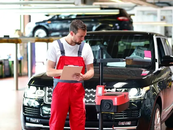 KFZ-Mechaniker prüft in Werkstatt ein Auto mit moderner Diagnoseausrüstung und Checkliste.