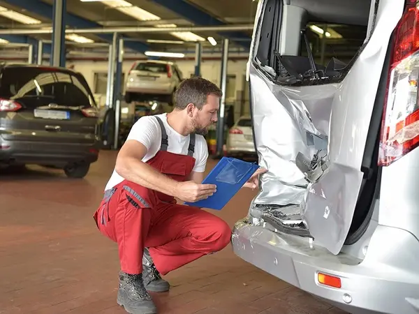 Ein Kfz-Gutachter prüft Unfallschaden an Auto in moderner Autowerkstatt.