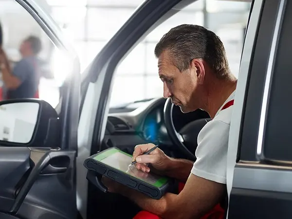 Automechaniker prüft Fahrzeuginformationen mit Diagnosegerät in moderner Autowerkstatt.