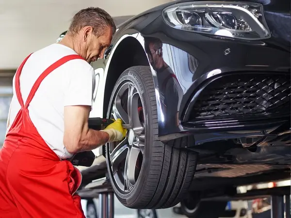 Mechaniker in roter Arbeitskleidung wechselt Reifen an schwarzem Auto in Werkstatt.