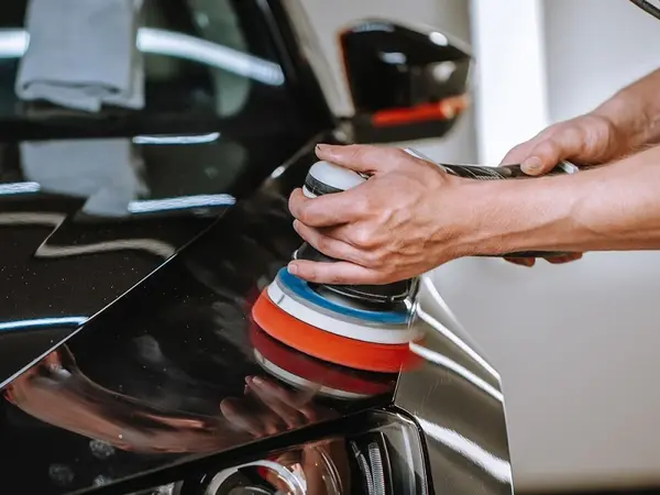 Eine Person poliert den schwarzen Autolack mit einer elektrischen Poliermaschine.